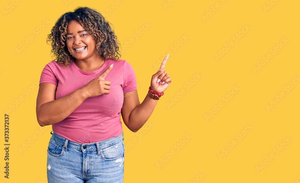 Young african american plus size woman wearing casual clothes smiling and looking at the camera pointing with two hands and fingers to the side.