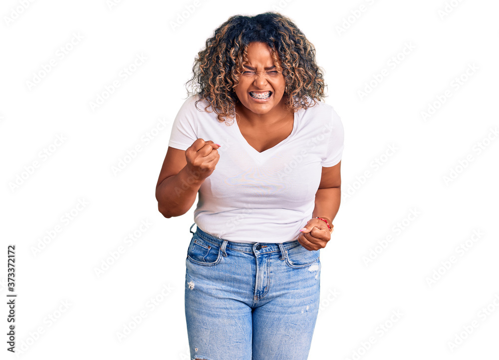 Young african american plus size woman wearing casual clothes angry and mad raising fist frustrated and furious while shouting with anger. rage and aggressive concept. Young african american plus size woman wearing casual clothes angry and mad raising fist frustrated and furious while shouting with anger. rage and aggressive concept.
