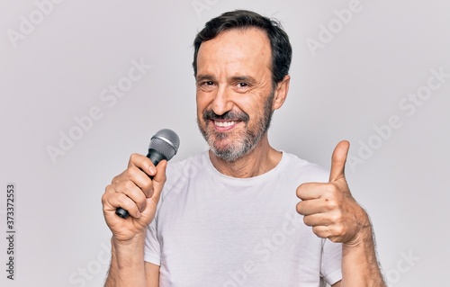 Middle age handsome singer man singing using microphone over isolated white background smiling happy and positive, thumb up doing excellent and approval sign
