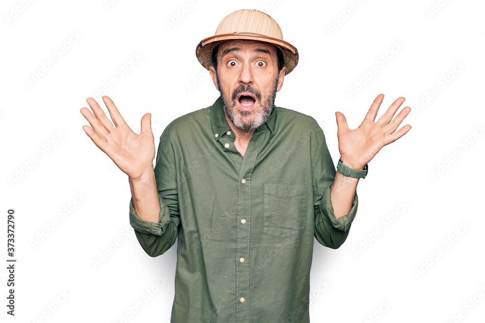 Middle age tourist man on vacation wearing explorer hat over isolated white background clueless and confused with open arms, no idea and doubtful face. Middle age tourist man on vacation wearing explorer hat over isolated white background clueless and confused with open arms, no idea and doubtful face.