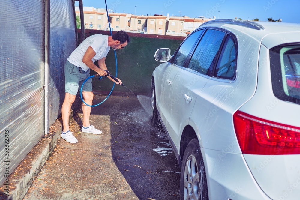 Middle age handsome man wearing casual clothes and sunglasses smiling happy. Standing with smile on face washing car using water pistol. Middle age handsome man wearing casual clothes and sunglasses smiling happy. Standing with smile on face washing car using water pistol.