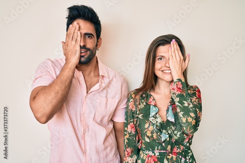 Beautiful young couple of boyfriend and girlfriend together covering one eye with hand, confident smile on face and surprise emotion.
