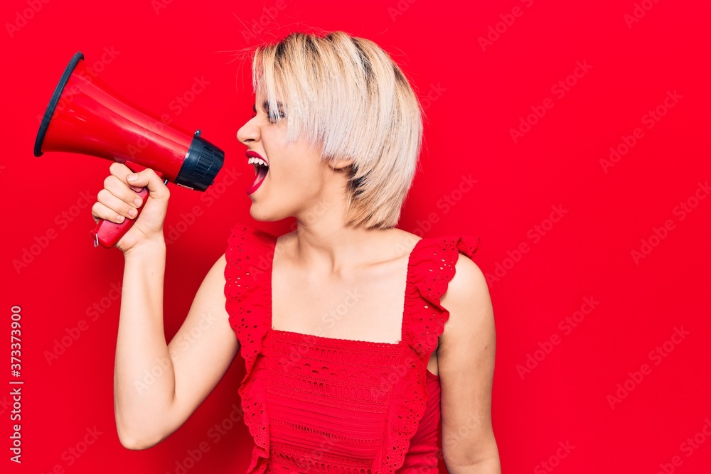 Young beautiful blonde woman with angry expression. Screaming loud using megaphone standing over isolated red background Young beautiful blonde woman with angry expression. Screaming loud using megaphone standing over isolated red background