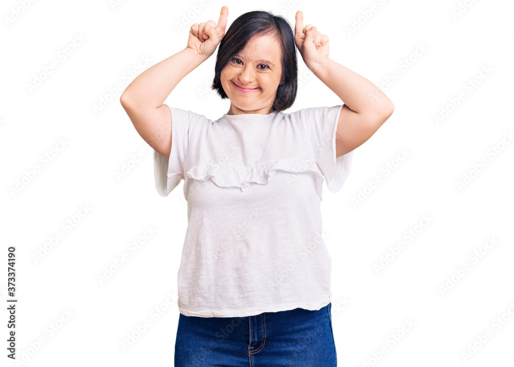 Brunette woman with down syndrome wearing casual white tshirt doing funny gesture with finger over head as bull horns Brunette woman with down syndrome wearing casual white tshirt doing funny gesture with finger over head as bull horns