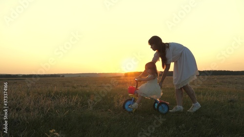 Mom teach a young child to ride a bike at sunset in the park. Teamwork. Silhouette family walk.