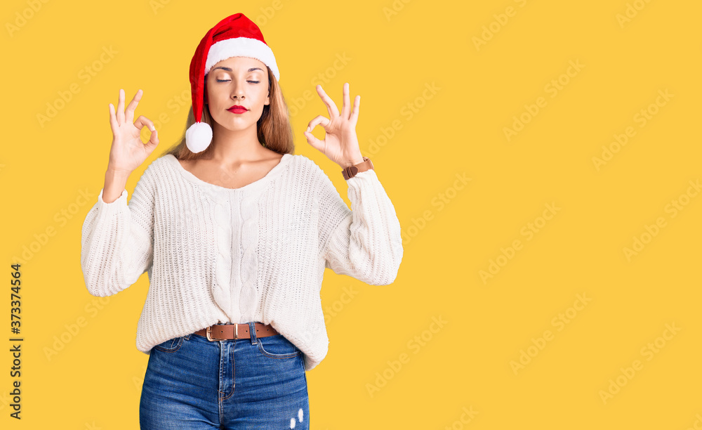 Beautiful young woman wearing christmas hat relax and smiling with eyes closed doing meditation gesture with fingers. yoga concept. Beautiful young woman wearing christmas hat relax and smiling with eyes closed doing meditation gesture with fingers. yoga concept.