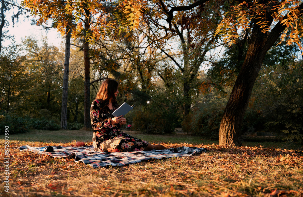 Artistic image, young woman sitting on blanket in the morning in park and reading a book Artistic image, young woman sitting on blanket in the morning in park and reading a book