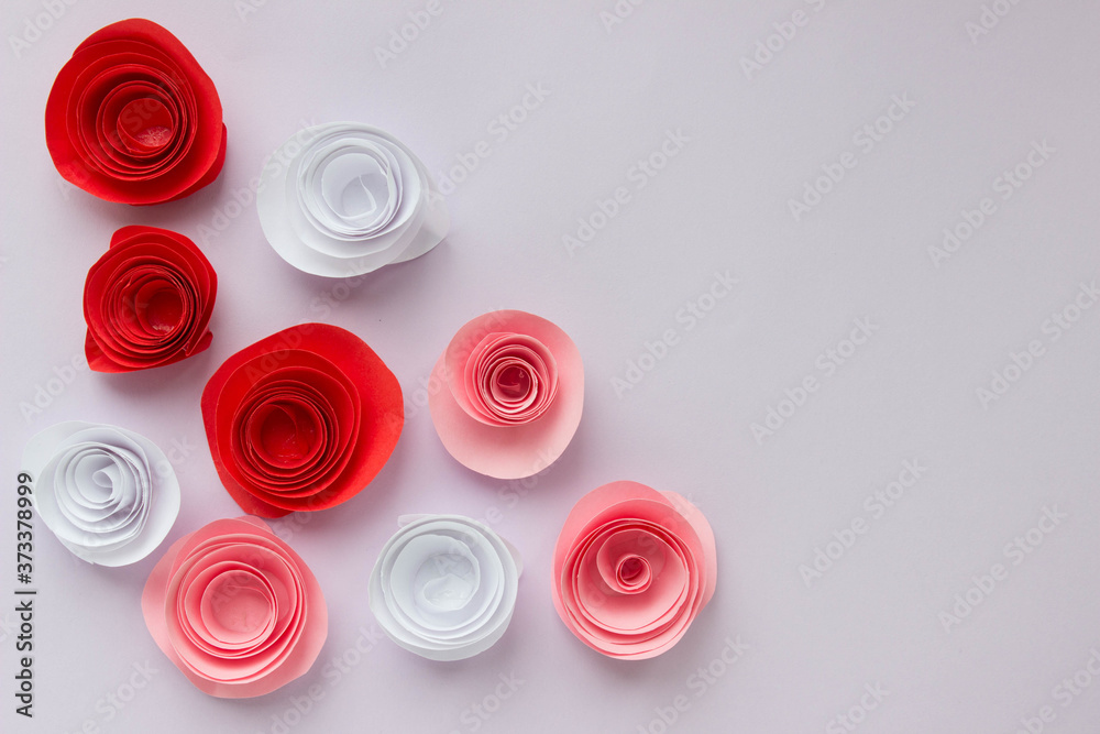 White, pink and red origami roses are scattered on a light background. With place for your design White, pink and red origami roses are scattered on a light background. With place for your design