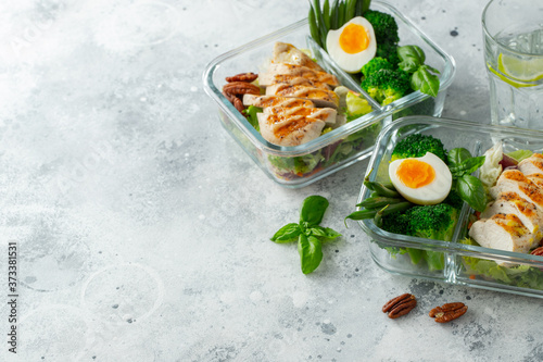 Healthy meal prep containers with green beans, chicken breast and broccoli. A set of food for keto diet in lunchbox on a light concrete background. Top view with copy space
