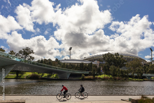 Two people cycling in front of the Adelaide Oval, sports stadium used for cricket, Australian football and rugby. Stadium built next to river Torrens (Karrawirra Parri). Adelaide, South Australia