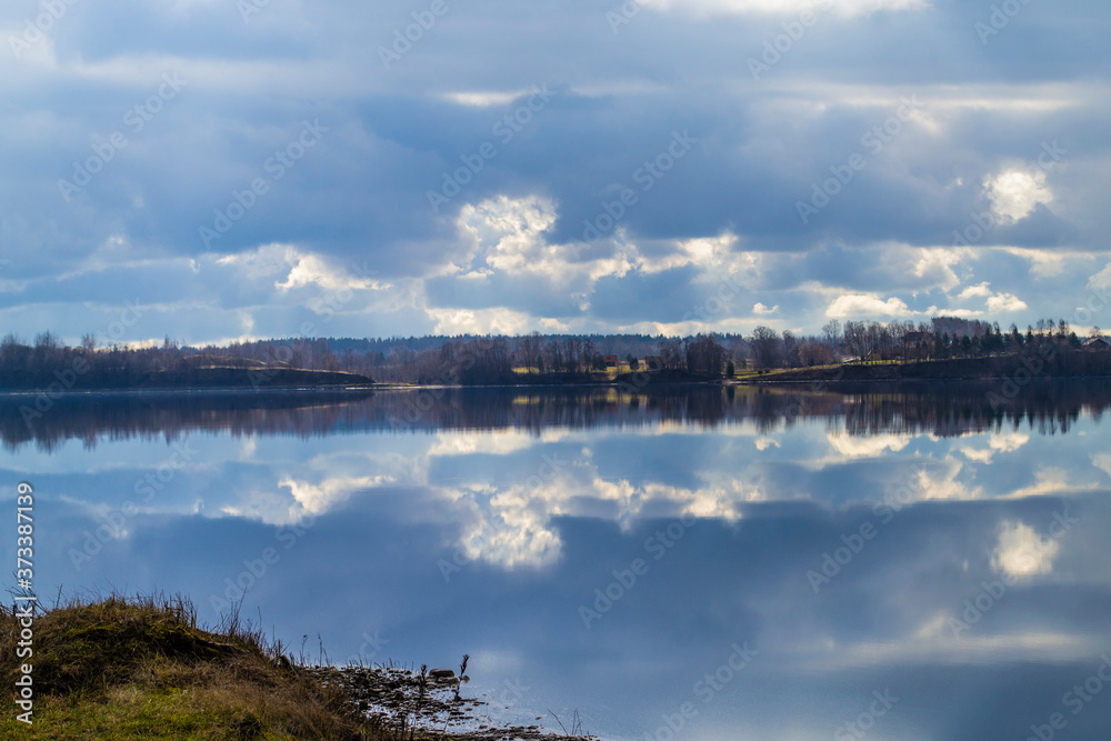 Rocky shore in the foreground. Picturesque view of the Daugava. The nature of Latvia. Beautiful clouds in the blue sky and reflected in the water.