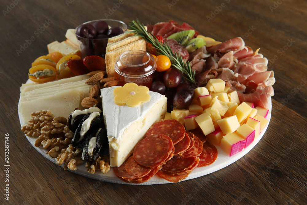 Brie, gouda, asiago, parmesan, cup, salami, jamon, apricots with gorgonzola, plums with cream chease and fruit. Antipasto dish on wooden table. Selective focus