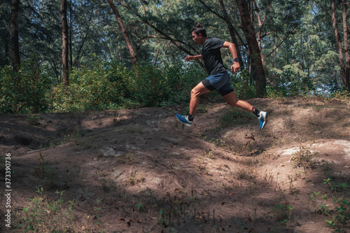 Motion of a man trail runner jumping over the hill while on running in the forest.
