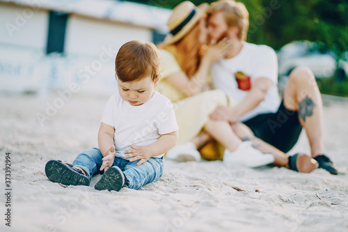 Beautiful red-haired woman with her husband and a wonderful son sitting on a summer beach on the sand © prostooleh