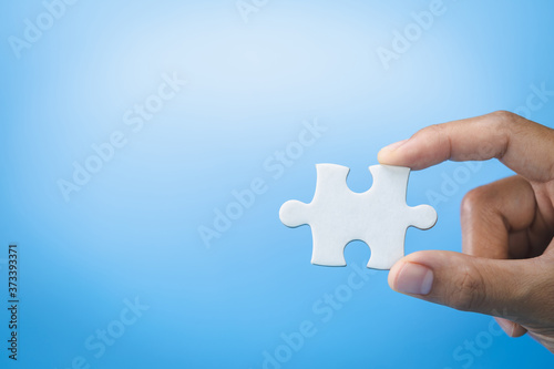 Hand holding jigsaw puzzleson a blue background, Business solutions, success and strategy concept.