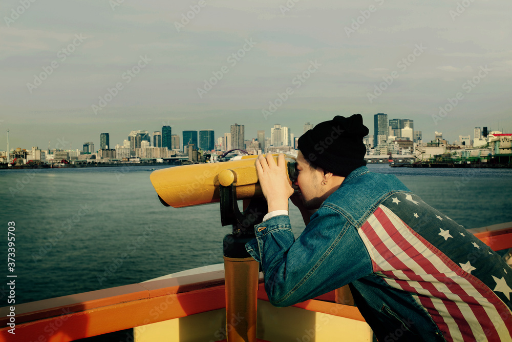 hipster man wearing american flag jeans jacket looking through binocular lens against urban building