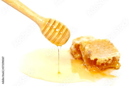 Honey dripping from wooden dipper with honeycomb isolated on white background.