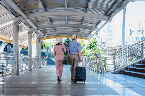Photography tourist older woman and man wearing casual dress , hand holding baggage for travel walking and talking passed the public sky walk bridge