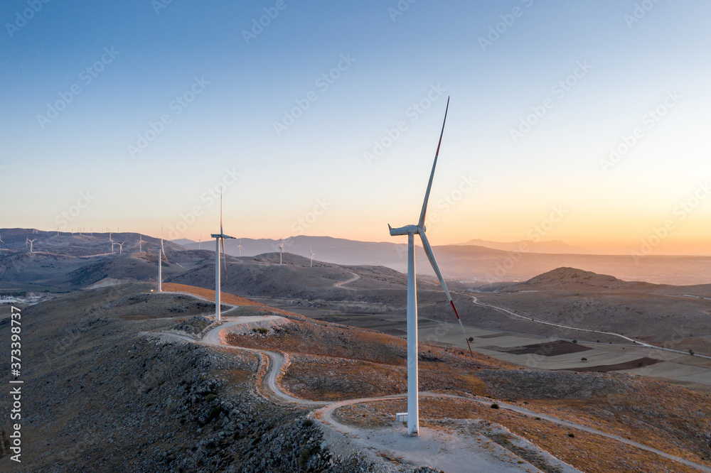 Wind power turbines generating electricity, Energy Production with clean. Mountains  and orange sunset in background, Aerial view from drone.