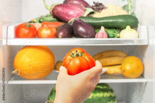 woman's hand picks up tomato from the refrigerator shelf. healthy food. healthy lifestyle concept