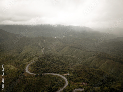 Logistic concept aerial view of countryside road - motorway passing through the serene lush greenery and foliage tropical rain forest mountain landscape