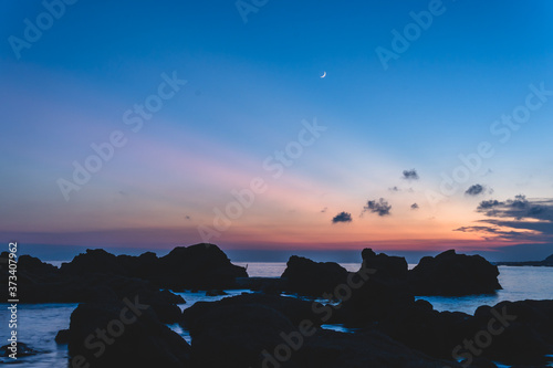 岩礁から望む水平線に沈む美しい夕焼けと月