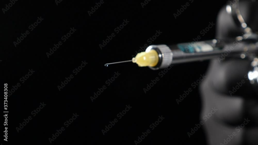 Dentist hand in black glove holding syringe with anesthesia Releasing Drug drop by drop. Usage of Sterile Equipment. Close-up shot of dentist holding syringe with anesthetic on black background. Full