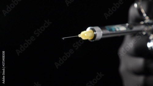 Dentist hand in black glove holding syringe with anesthesia Releasing Drug drop by drop. Usage of Sterile Equipment. Close-up shot of dentist holding syringe with anesthetic on black background. Full