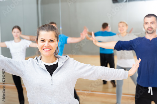Smiling young female coach doing dance workout with adult group in fitness center