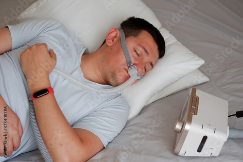 Close-up of young adult man wearing under the nose nasal mask ( CPAP mask ) and using CPAP machine for sleeping smooth without snoring.