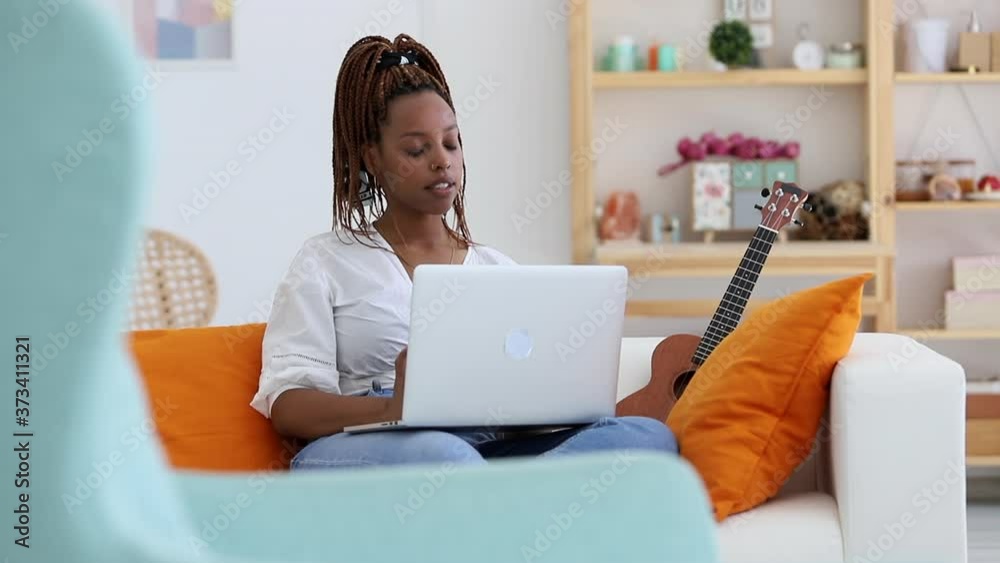 African American woman working with laptop remotely, sitting on couch in apartment interior spbi. Attractive girl looking at computer screen with smile and thinking on sofa in light room. Pretty African American woman working with laptop remotely, sitting on couch in apartment interior spbi. Attractive girl looking at computer screen with smile and thinking on sofa in light room. Pretty