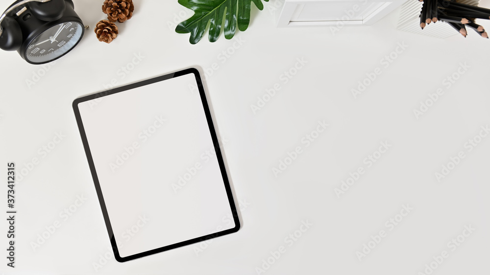 Top view of blank screen tablet on desk with clock, pine cone, frame photo and pencils on white background. Top view of blank screen tablet on desk with clock, pine cone, frame photo and pencils on white background.
