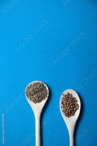 two wooden spoons of coriander and cumin on blue background flat lay. Image contains copy space