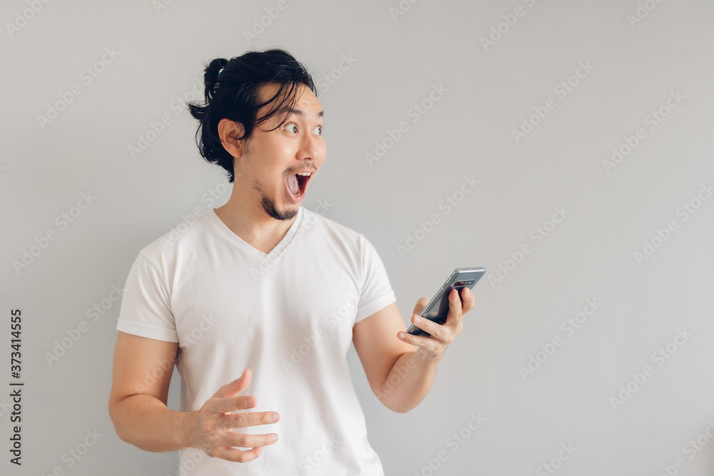 Surprised and shocked long hair Asian man in white t-shirt is using smartphone. Surprised and shocked long hair Asian man in white t-shirt is using smartphone.