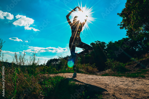 Woman Doing Yoga On Mountain Against Sky and Sun. Hard light. Silhouette of girl doing outdoor sport stretch. photo