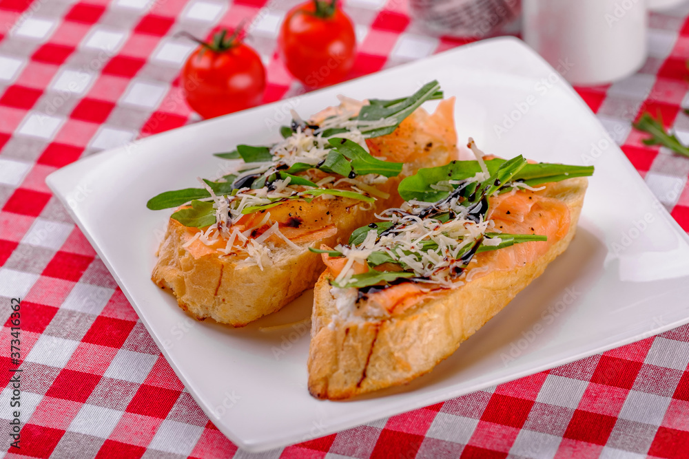 Italian Appetizer Bruschetta with Salmon, parmesan, balsamic vinegar and fresh arugula on white plate in italian restaurant background, top view. Italian Appetizer Bruschetta with Salmon, parmesan, balsamic vinegar and fresh arugula on white plate in italian restaurant background, top view.