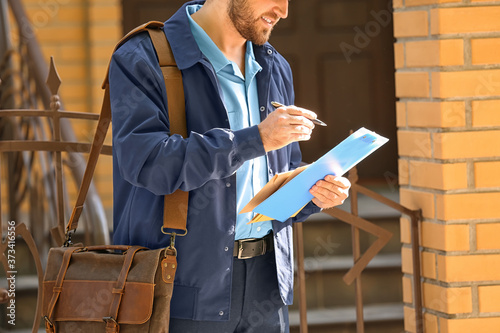 Handsome young postman with letters outdoors