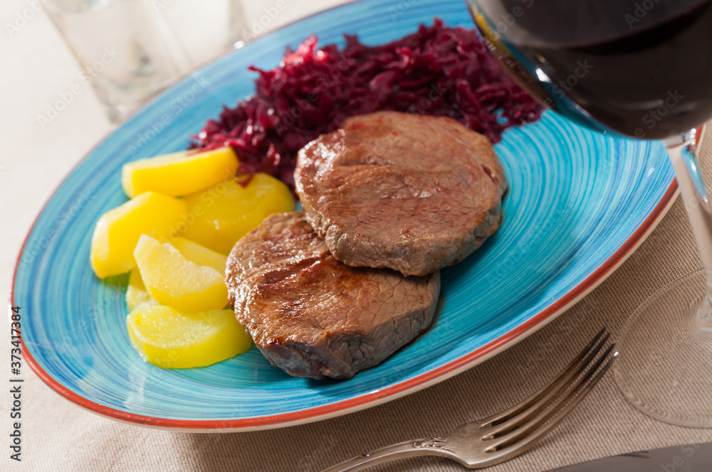 Appetizing roasted beef steaks served with baked potatoes and pickled cabbage..