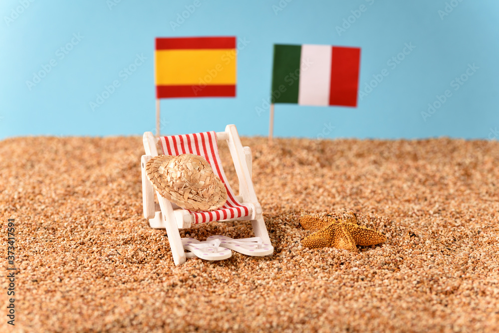 Sunbed on the beach with Spanish and Italian flag on the blurred background. Sunbed on the beach with Spanish and Italian flag on the blurred background.