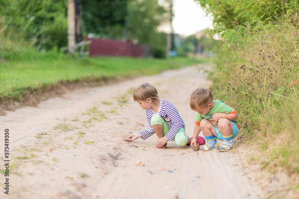 Children draw with a stone on the sand while squatting on a sandy village road Children draw with a stone on the sand while squatting on a sandy village road