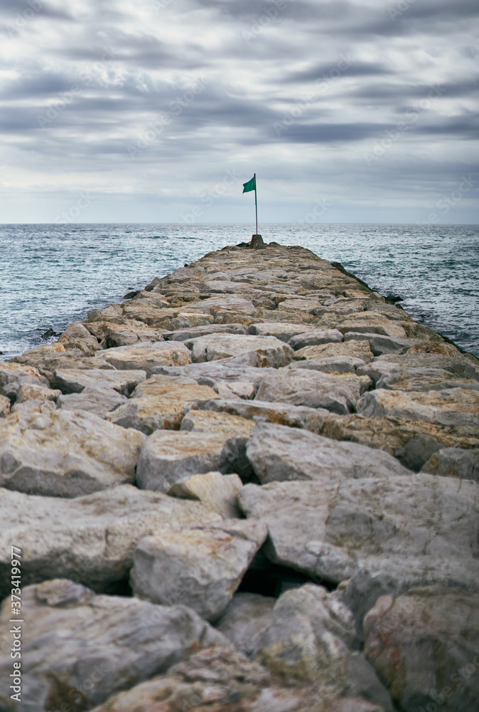 Breakwater of rocks with a green flag at the end
