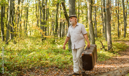Grandfather with vintage suitcase in nature. United with nature. Weekend in nature. Mature man with white beard in forest. Hobby and leisure. Elderly people. Vacation and relax. Retirement concept