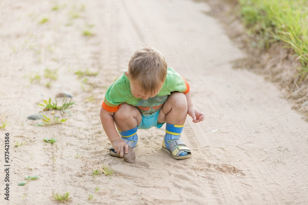 Boy draws with a stone on the sand while squatting on a sandy village road Boy draws with a stone on the sand while squatting on a sandy village road
