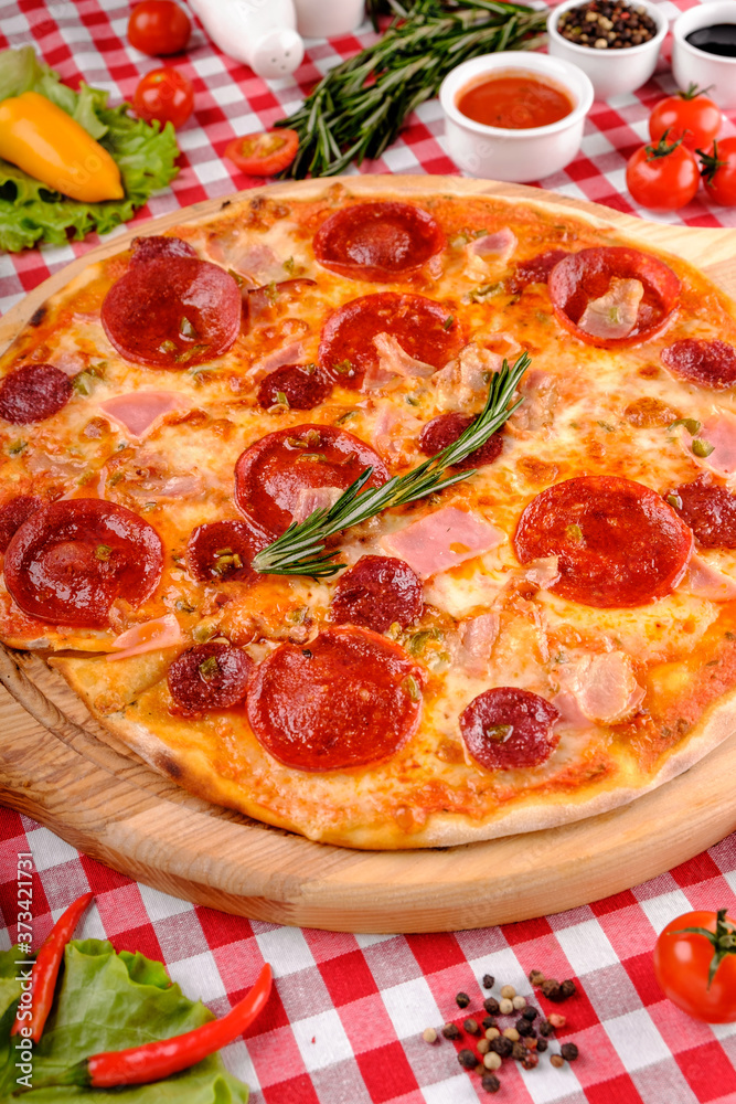 Neapolitan Pepperoni pizza with sausage, salami, cheese, rosemary and tomatoes sauce, served on a wooden board for a dinner in italian restaurant background, top view. Italy food. 