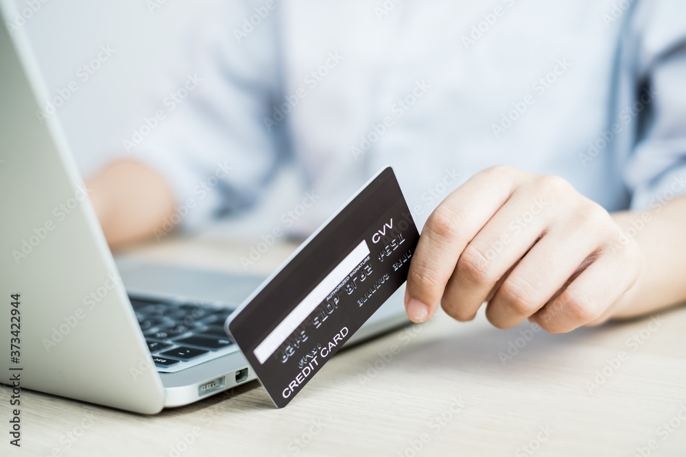The businesswoman's hand is holding a credit card and using a laptop for online shopping and internet payment in the office The businesswoman's hand is holding a credit card and using a laptop for online shopping and internet payment in the office