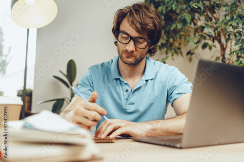 Young man in blue shirt sits at the table and studies with laptop