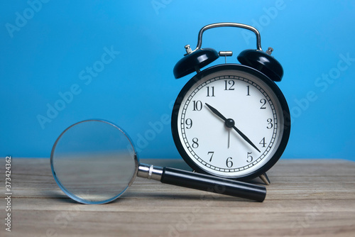Selective focus of vintage alarm clock and magnifying glass on wooden table with a blue background.