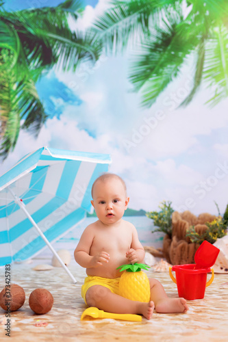 Happy little boy sunbathing on a sandy beach by the sea with palm trees under a beach umbrella