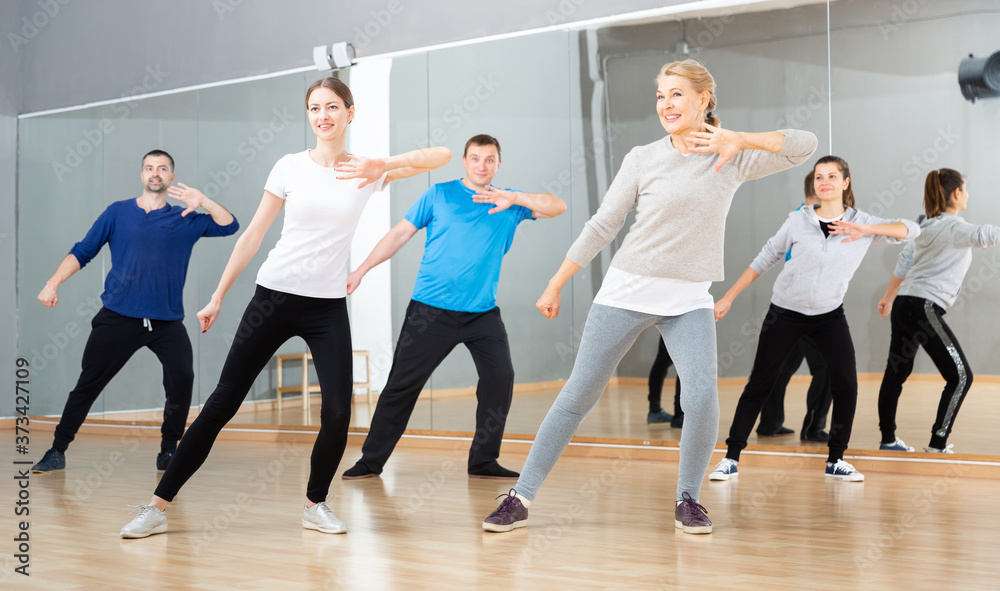 Fototapeta premium Sporty females and males doing stretching workout during group training at dance class
