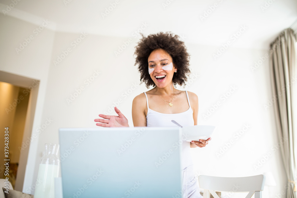 Beautiful young woman enjoys eating corn flakes for breakfast while working on her laptop in the morning. Looking at laptop computer and talking to her friends via video call. Beautiful young woman enjoys eating corn flakes for breakfast while working on her laptop in the morning. Looking at laptop computer and talking to her friends via video call.